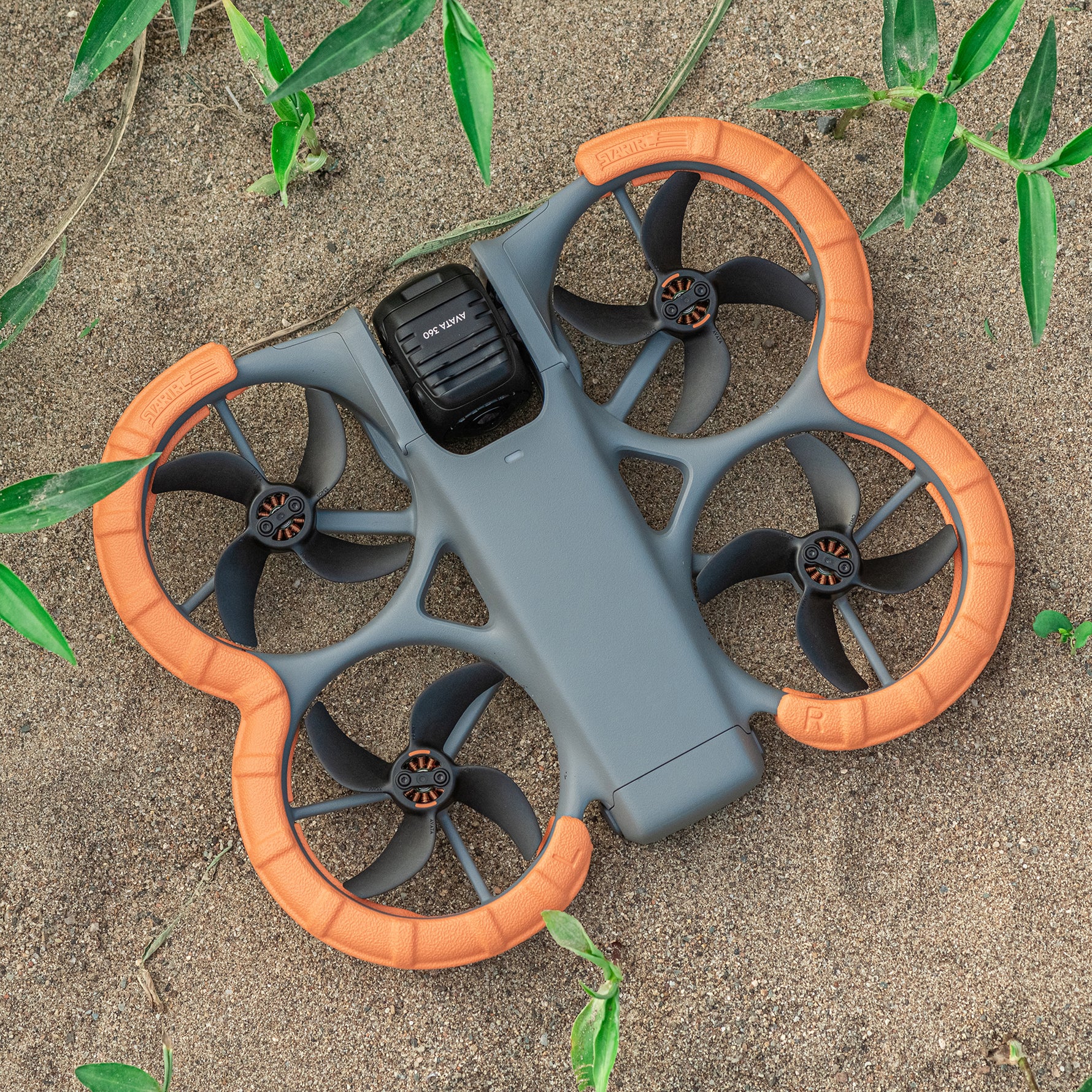 DJI Avata 360 landed in dirt. The high-visibility orange STARTRC drone guards ensure effortless drone retrieval in grass or forests.