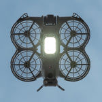Bottom view of the DJI Neo 2 in flight, showcasing the LED landing gear acting as a powerful fill light to improve shooting quality in low-light environments.