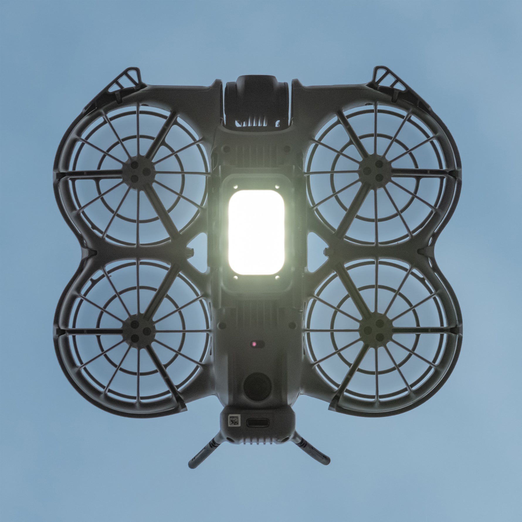 Bottom view of the DJI Neo 2 in flight, showcasing the LED landing gear acting as a powerful fill light to improve shooting quality in low-light environments.