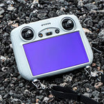 DJI RC controller resting on rough outdoor gravel with the rugged screen shield installed, boasting superior resistance to scratches from sand and debris.