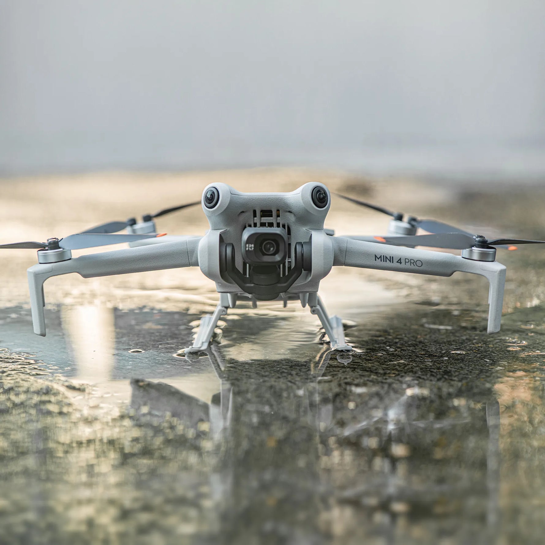 Camera drone equipped with the slope landing gear safely parked on a wet outdoor surface, protecting the gimbal and fuselage from water damage.