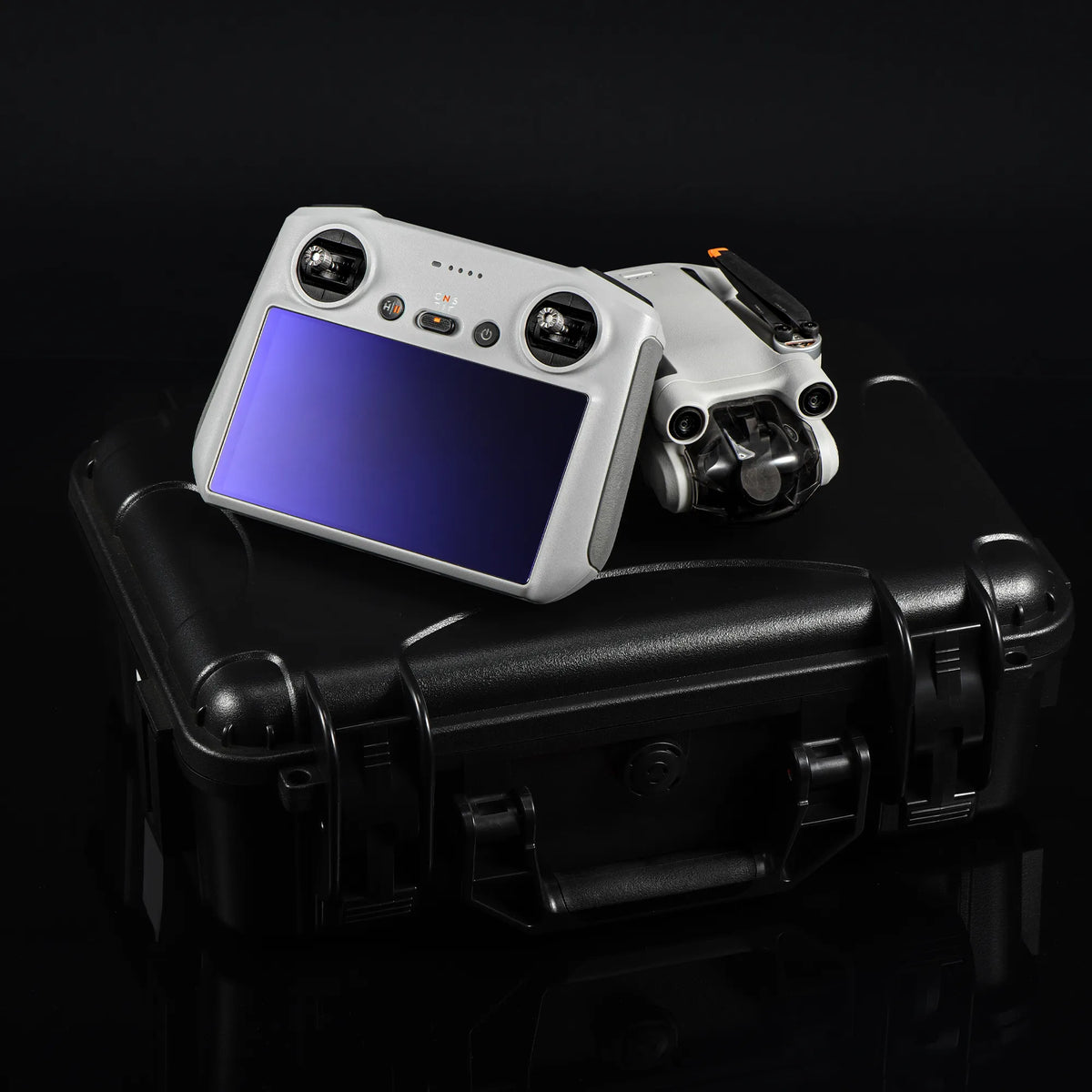 A DJI RC remote controller resting on a rugged hard case outdoors, protected by the STARTRC explosion-proof screen guard against scratches from sand and keys.