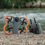DJI Avata 360 equipped with STARTRC EVA bumper guards resting on gravel near water, alongside the remote controller. Essential DJI Avata 360 accessories for outdoor protection.