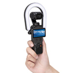 A hand holding the DJI Osmo Pocket equipped with the STARTRC magnetic ring light, demonstrating zero obstruction of the screen and gimbal.